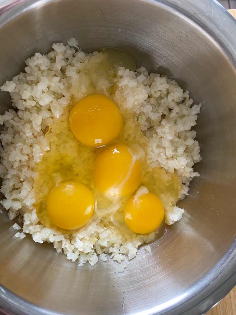 riced cauliflower with raw eggs in mixing bowl