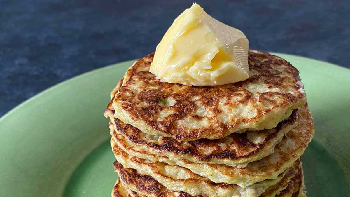 stack of cauliflower pancakes with butter on a green plate and blue background