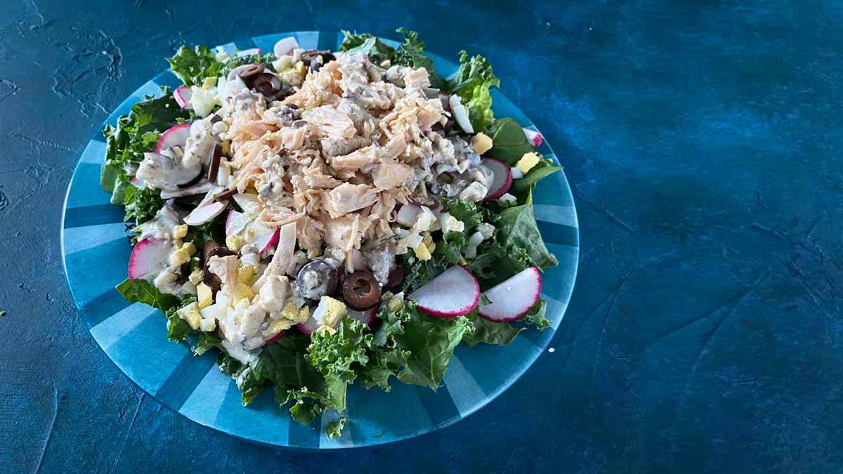 keto friendly salad with greens, chicken, olives, radishes, and keto friendly dressing on plate