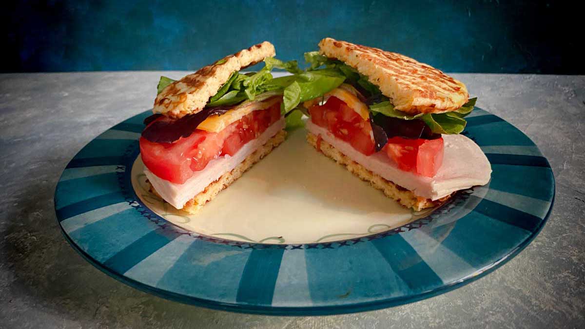 sandwich on plate made from chaffle bread, turkey, cheese, tomatoes and greens
