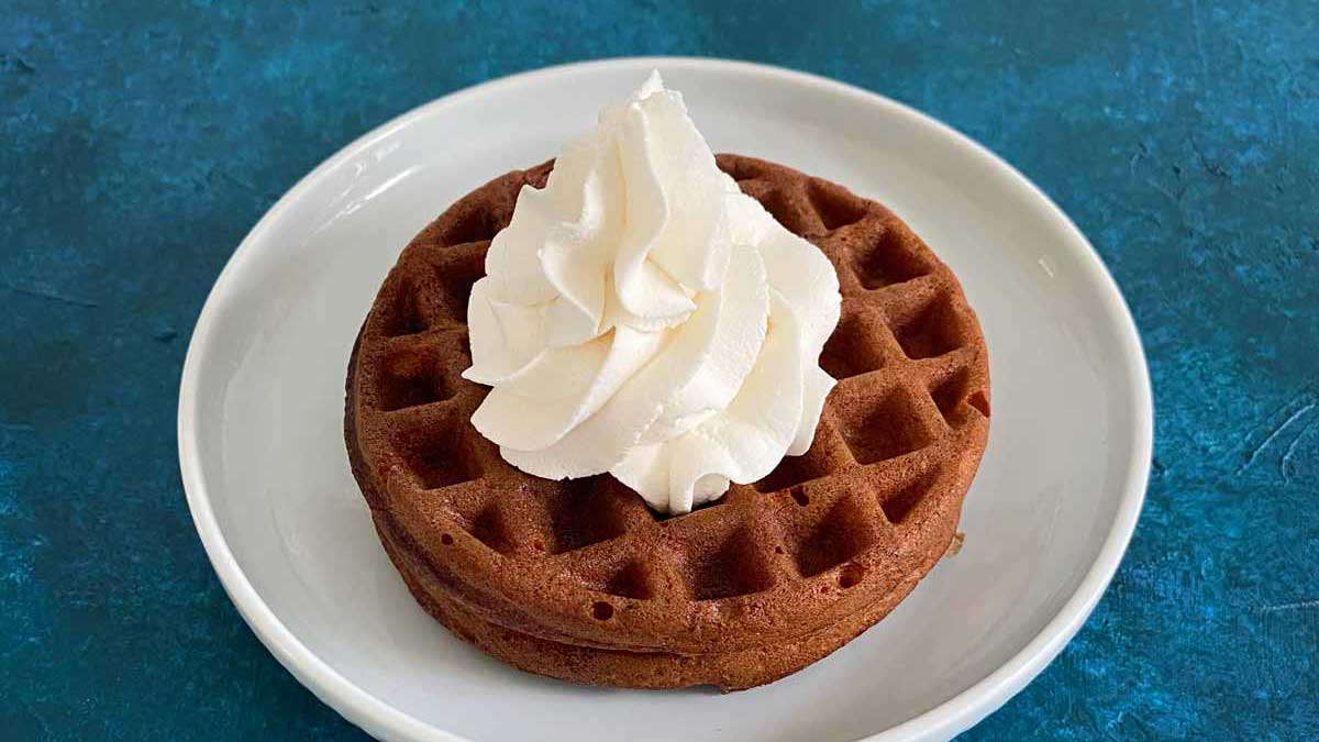 chocolate chaffle with whipped cream on a white plate and blue background