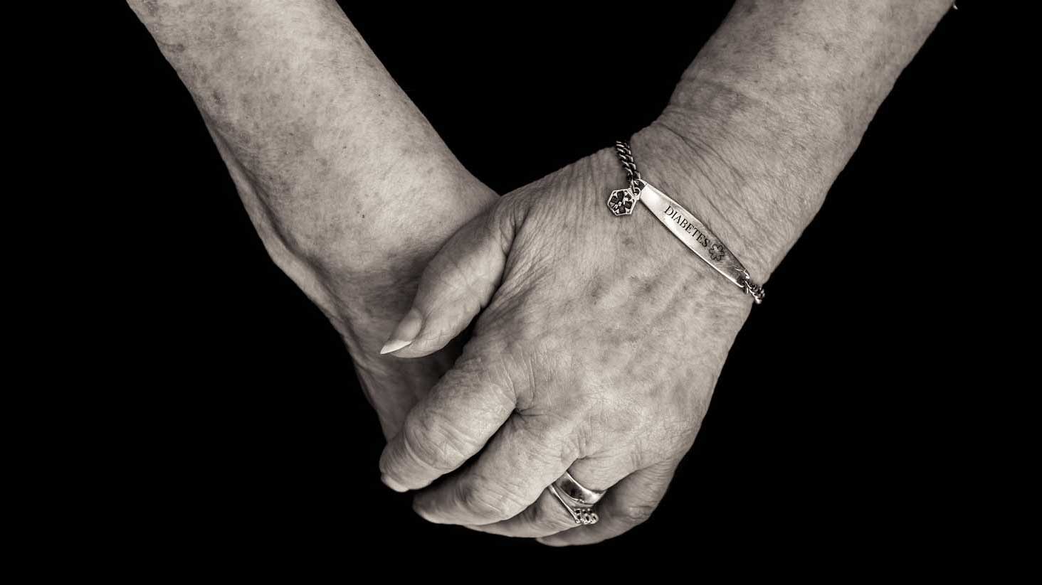 folded elderly hands with medical alert bracelet